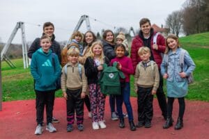 A group of 12 children and young adults pose with their Heirs Backpacks in a park