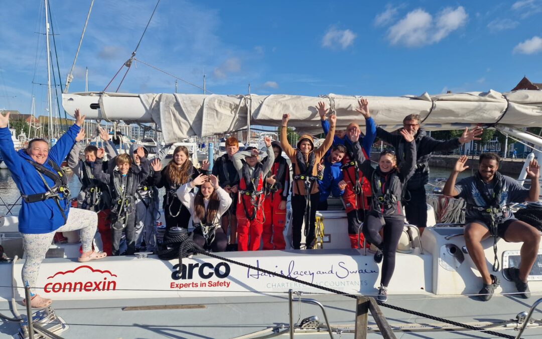 A team of cheering young people on deck the CatZero Yacht on a sunny day in the harbour