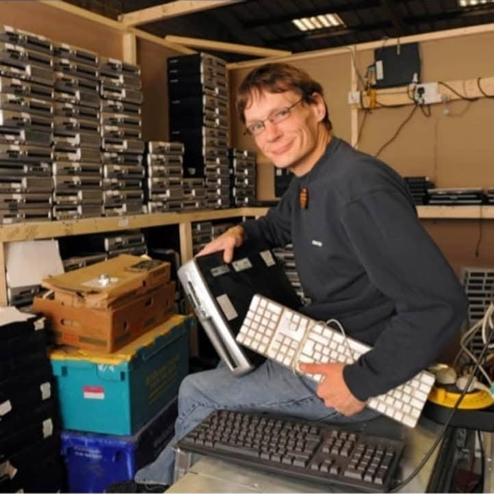 John from Recycle-IT! smiles at the camera as he sorts through some IT recycling goods in the Bolton store